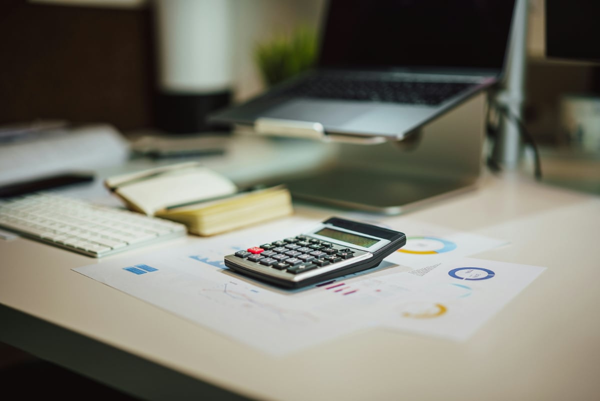 a calculator on some bills on a desk in front of a computer on a stand.