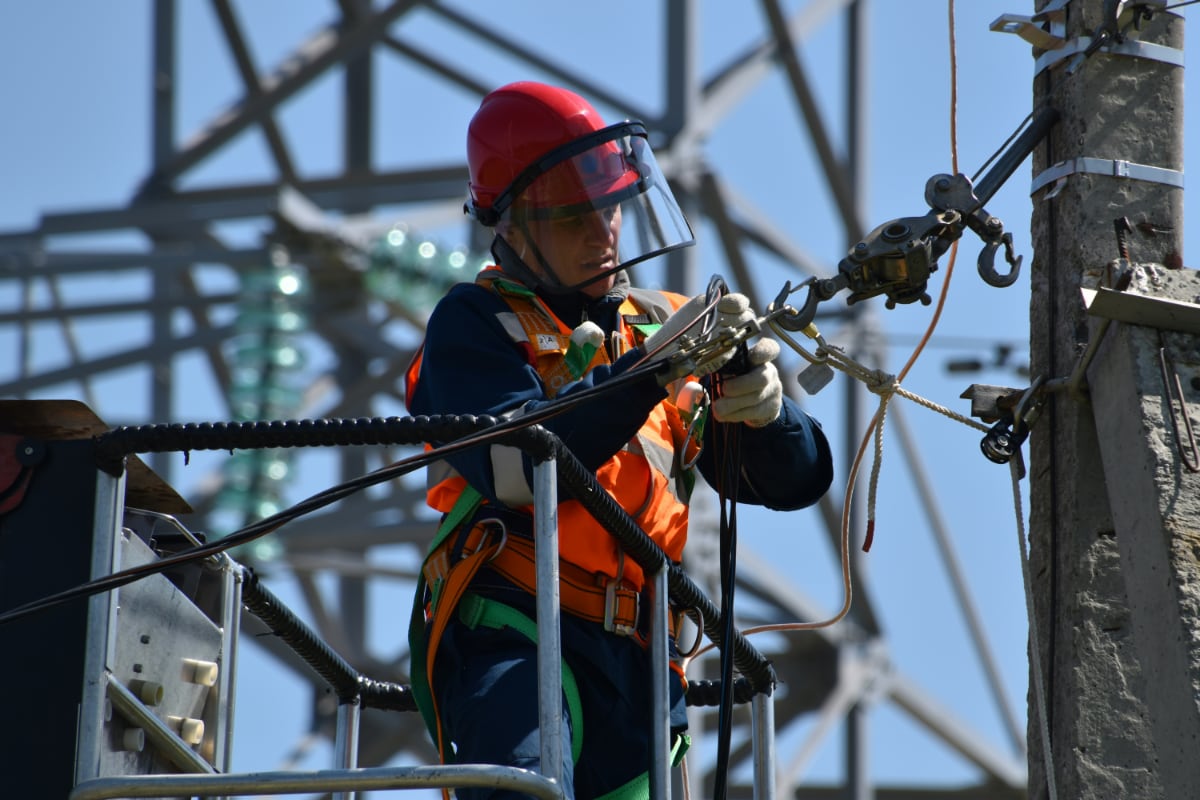 A person working on an electric power pole in a hi-vis vest and a face shield